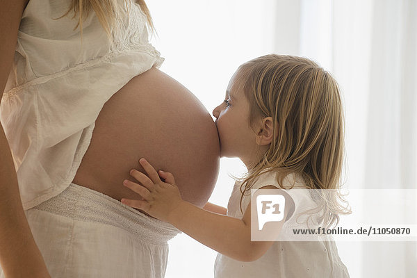 Kaukasisches Mädchen küsst den Bauch der schwangeren Mutter