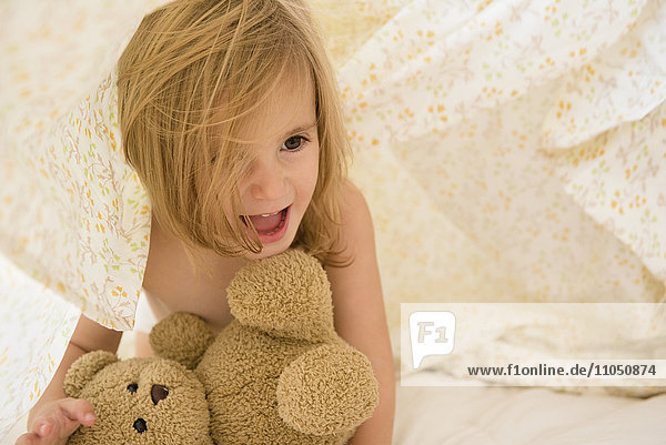 Kaukasisches Mädchen spielt mit Teddybär unter Decken