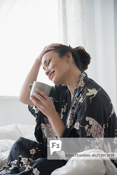 Woman drinking cup of coffee on bed
