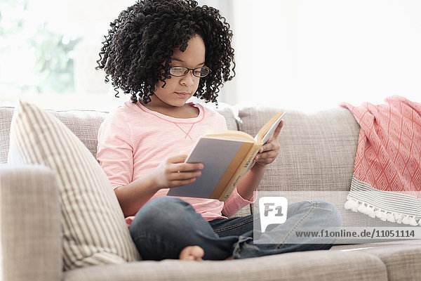 African American girl reading book on sofa