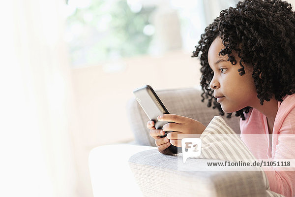 Afroamerikanisches Mädchen benutzt Mobiltelefon auf dem Sofa