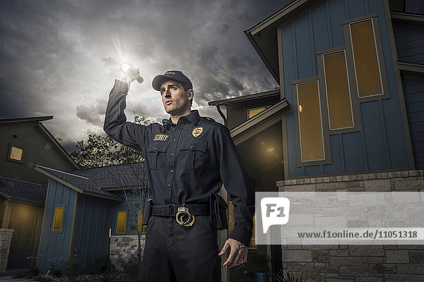 Weißer Polizist leuchtet mit einer Taschenlampe in der Nähe eines Hauses