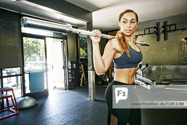 Mixed Race woman stretching with barbell in gymnasium