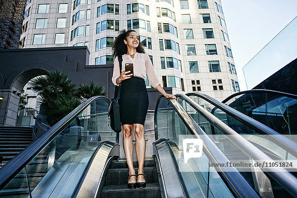 Smiling Hispanic businesswoman riding escalator outdoors