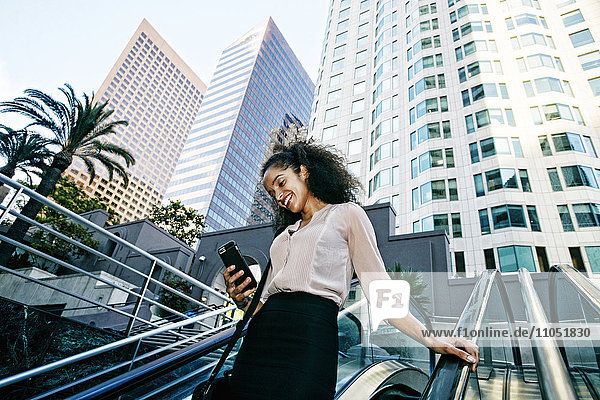 Smiling Hispanic businesswoman texting on escalator outdoors