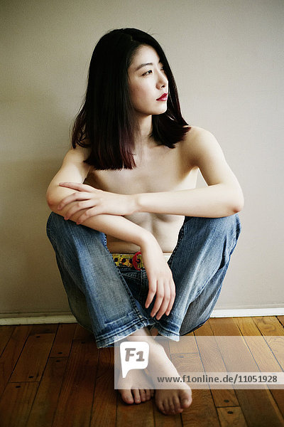 Topless asiatische Frau sitzt auf dem Boden lehnt an der Wand