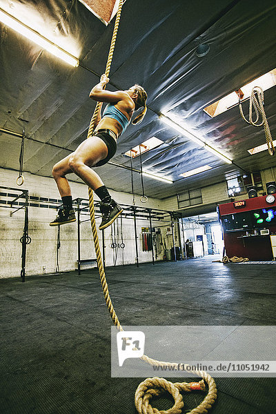 Caucasian woman climbing rope in gymnasium