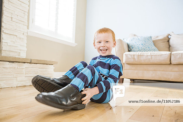 Kaukasischer Junge trägt Schuhe des Vaters im Wohnzimmer