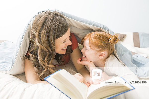 Kaukasische Mutter und Tochter lesen ein Buch im Bett