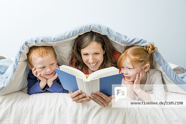 Caucasian mother and children reading book in bed