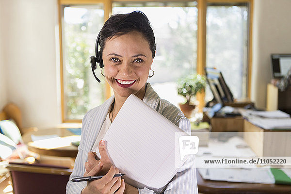 Geschäftsfrau mit Notizblock und Headset im Büro