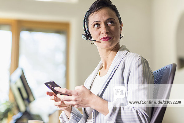 Geschäftsfrau mit Mobiltelefon und Headset im Büro