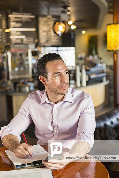 Hispanic businessman using cell phone in coffee shop