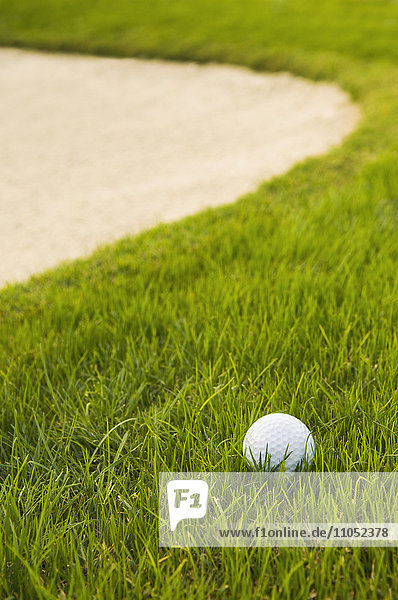 Nahaufnahme eines Golfballs in der Nähe eines Sandlochs auf einem Golfplatz