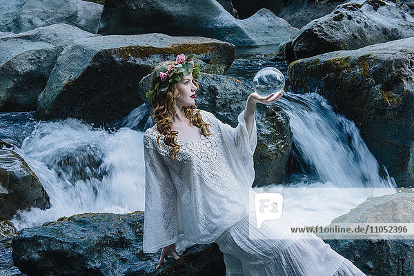 Kaukasische Frau hält Kristallkugel am Flusswasserfall