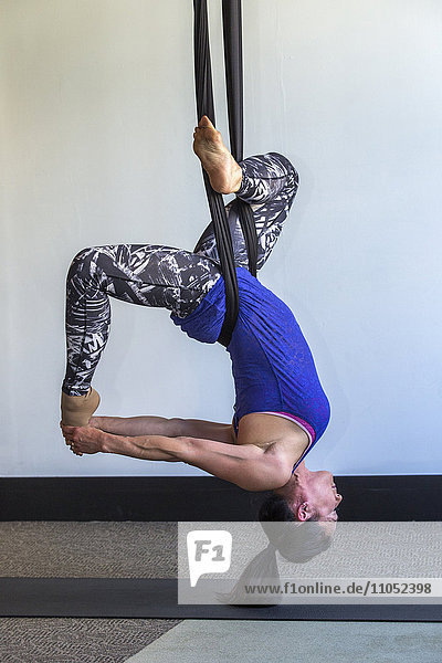 Gemischtrassige Frau  die an Seilen hängend Yoga praktiziert