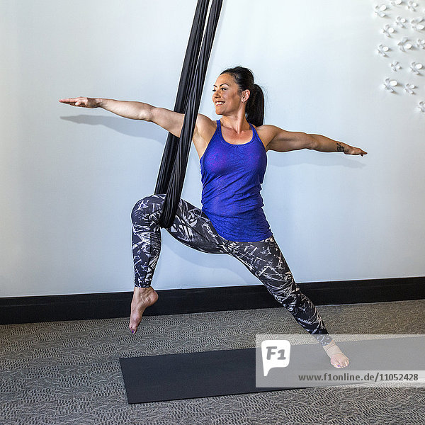 Gemischtrassige Frau beim Yoga an Seilen hängend