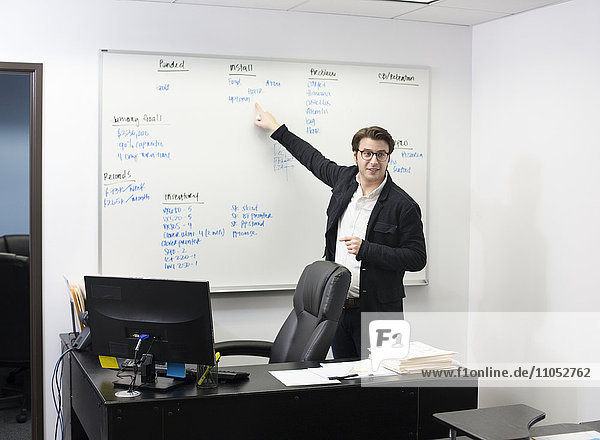 Kaukasischer Geschäftsmann  der auf ein Whiteboard im Büro zeigt