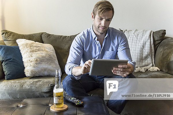 Mann benutzt digitales Tablet auf Sofa