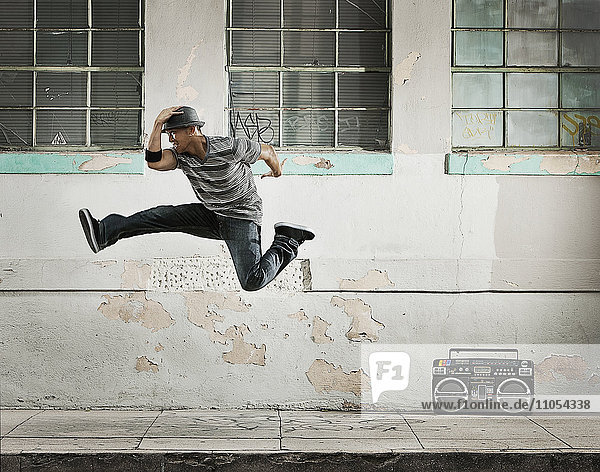 A young man breakdancing  leaping in the air doing a karate kick on a city street.