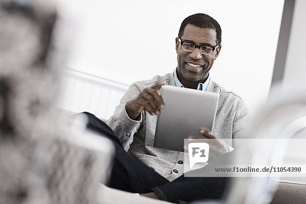 Ein Mann sitzt auf einem Sofa und benutzt ein digitales Tablett.