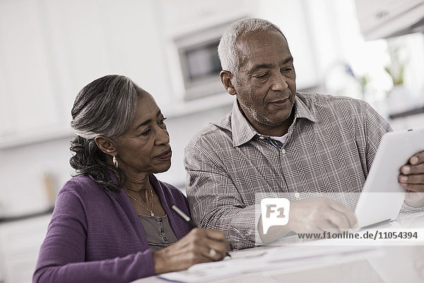 Ein älteres Ehepaar sitzt nebeneinander an einem Tisch  benutzt ein digitales Tablett und schaut auf den Bildschirm.