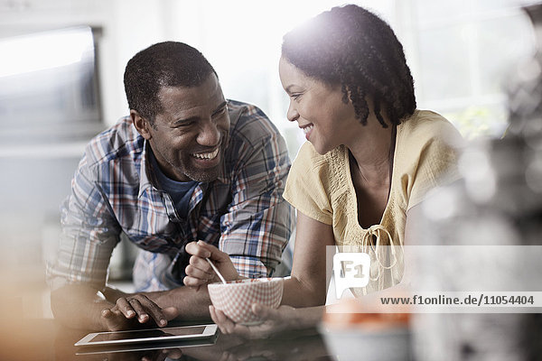 Ein Mann und eine Frau  ein Paar in der Küche  die beide auf ein digitales Tablet schauen.