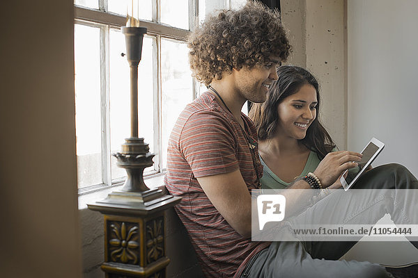 Loft-Wohnen. Ein Mann und eine Frau sitzen am Fenster und benutzen ein digitales Tablett.