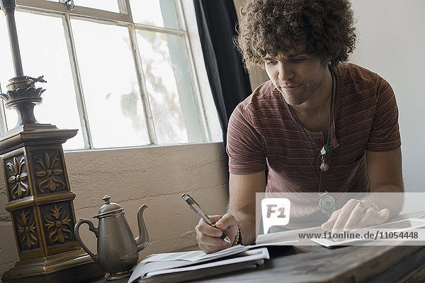 Loft-Wohnen. Ein Mann am Fenster sitzend  mit Stift und Papier und einem digitalen Tablett.