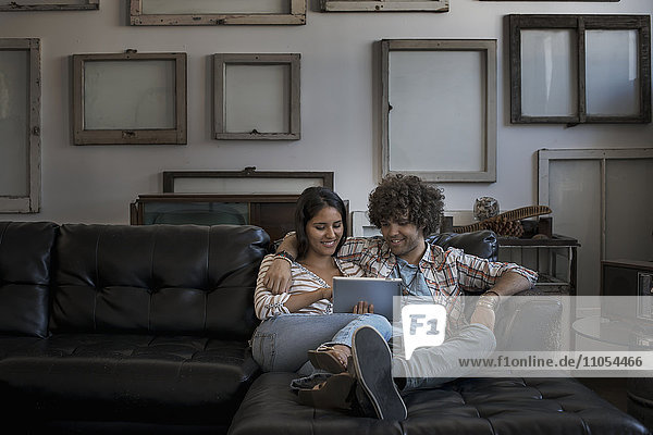 Loft decor. A wall hung with pictures in frames  reversed to show the backs. A couple on a sofa  looking at a digital tablet.