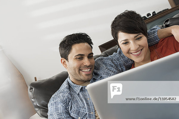 A man and woman sitting on a sofa  looking at the screen of a laptop.