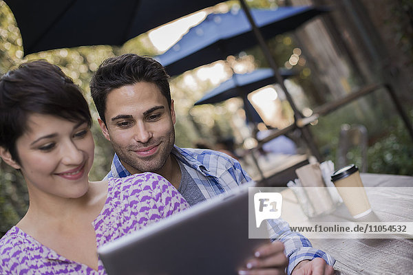 A couple man and woman sitting at an outdoor cafe sharing a digital tablet.