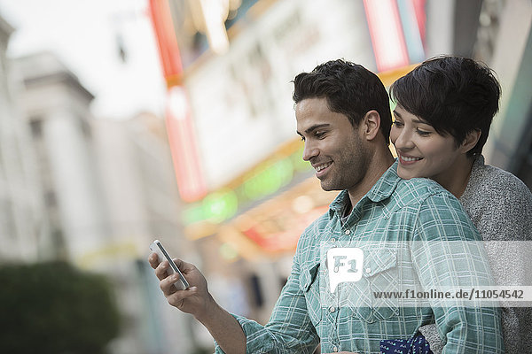A couple  man and woman hugging on a city street. Man holding a smart phone.
