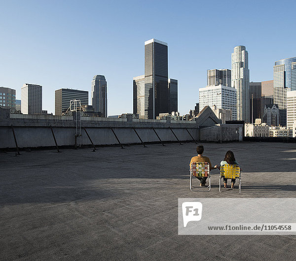 Ein Paar  Mann und Frau  die in Liegestühlen auf einem Dach mit Blick auf die Wolkenkratzer der Stadt sitzen.