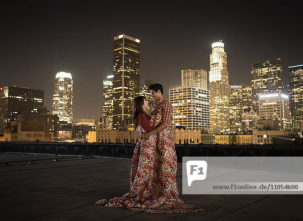A couple on a rooftop overlooking Los Angeles at night  warpped in blankets.