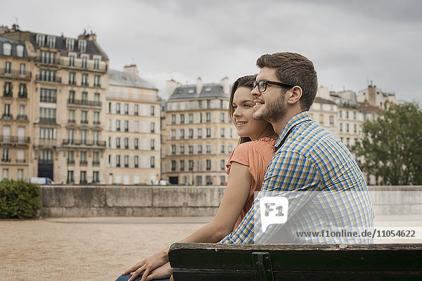 A couple  man and woman sitting close together on a bench by the River Seine.