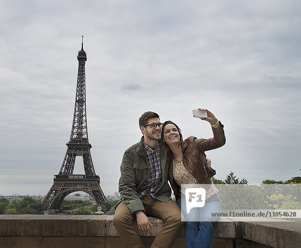 Ein Paar  das nebeneinander sitzt und ein Selfy mit dem Eiffelturm im Hintergrund nimmt.