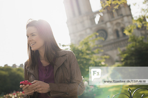 Eine Frau schaut mit einem Smartphone in der Hand in die Ferne vor der Kathedrale Notre Dame in Paris.