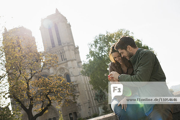Ein Ehepaar nebeneinander auf dem Bildschirm eines Smartphones vor der Kathedrale Notre Dame in Paris.