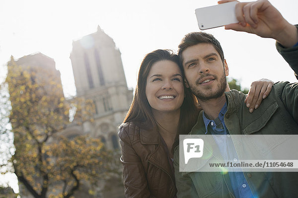 Ein Mann hält ein Smartphone in der Hand und nimmt sich und seine Freundin vor der Kathedrale Notre Dame in Augenschein.