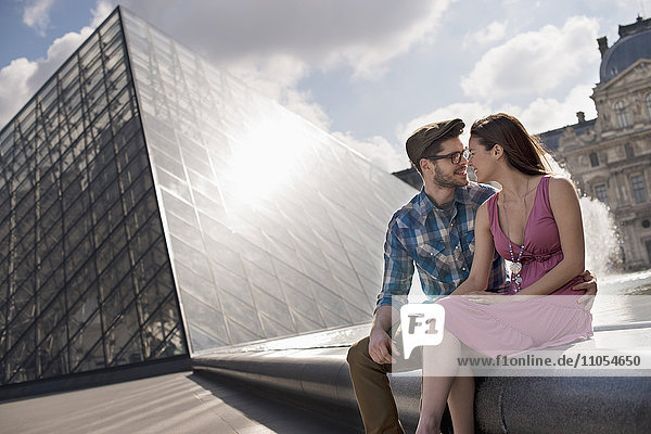 Ein Ehepaar sitzt am Wasserbecken im Innenhof des Louvre bei der großen Glaspyramide.