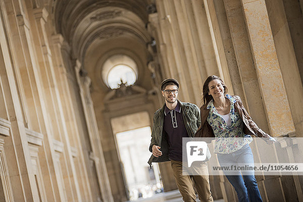 Ein junges Paar geht eine Kolonnade im historischen Herzen einer Stadt hinunter.
