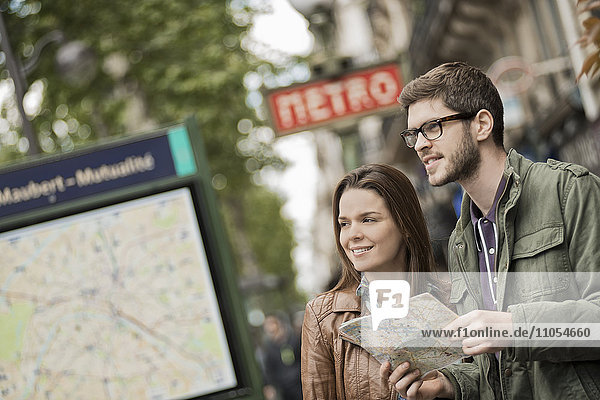 Ein Ehepaar  das einen Stadtplan neben einem Informationsschild unter einem U-Bahn-Schild in einer Stadt benutzt.