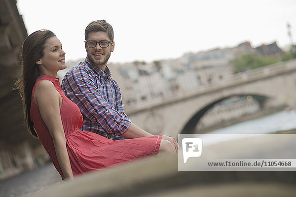 Ein Ehepaar in einer Stadt am Ufer des Flusses  das auf einer Kaibank sitzt.