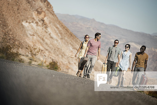 A group of people walking in a line in open desert country  carrying their cases  on a road trip.