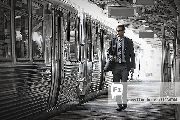 Ein Arbeitstag. Geschäftsmann in Arbeitsanzug und Krawatte  der mit einem Zugwaggon auf den Bahnsteig geht.