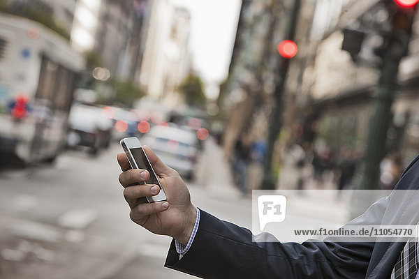 Ein Arbeitstag. Geschäftsmann in Arbeitsanzug und Krawatte auf einer Straße in der Stadt  der sein Telefon überprüft.