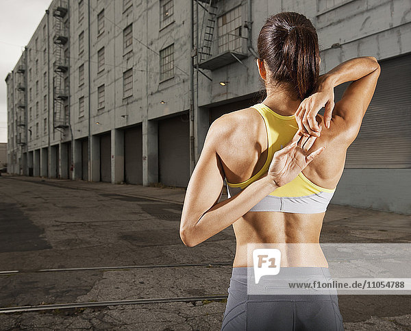 Eine Frau in Laufbekleidung  Korboberteil und Shorts  die ihren Körper streckt  sich nach dem Training abkühlt und ihre Hände hinter dem Rücken zusammenbindet.