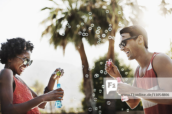 Zwei Personen blasen Blasen mit Hilfe von Blasenstäben.