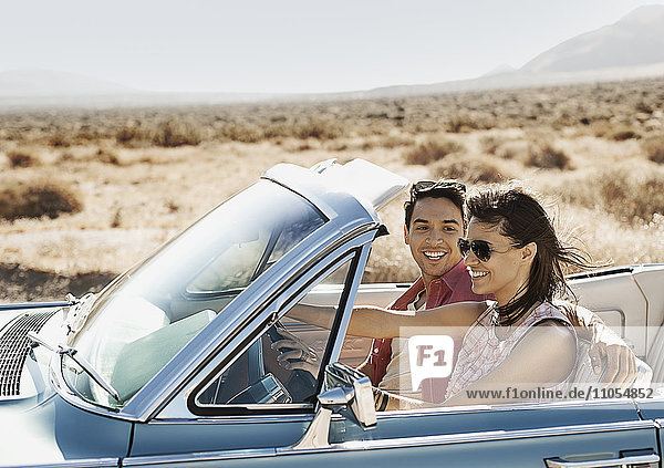 Ein junges Paar  Mann und Frau in einem hellblauen Cabriolet auf offener Straße